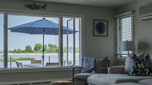 A living room with a large window, a blue umbrella, a sofa, and a chair. - Riverfront Shore House w/ Ocean View, Private Beach, 6 Bedrooms and Lots of Toys (Brielle)