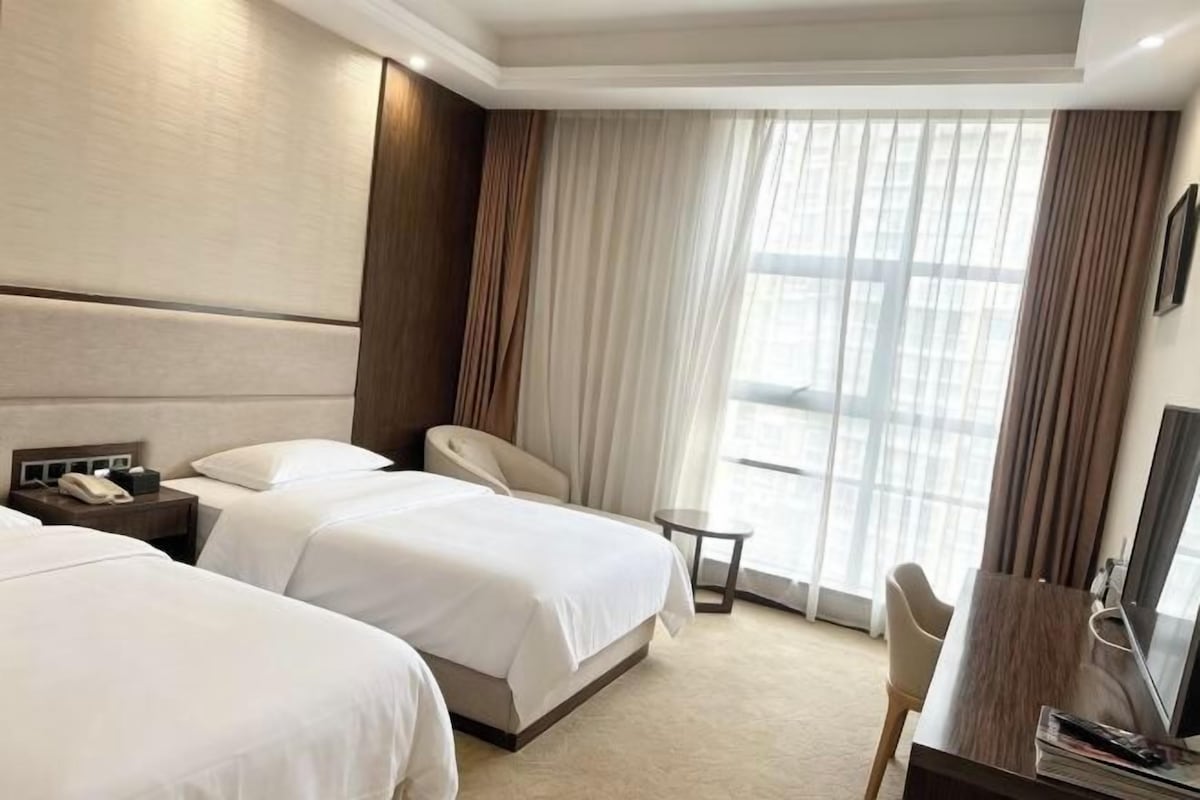 A hotel room with two beds, a desk, a chair, a TV, and a window with curtains.