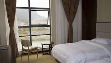 A hotel room with a large window, a bed, a chair, and a small table.