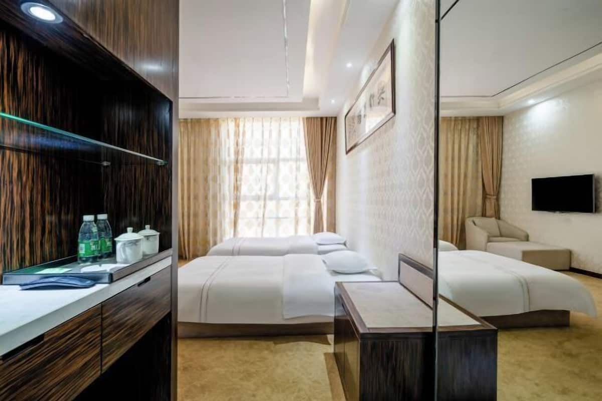A hotel room with two beds, a desk with toiletries, a TV, and a large window with curtains.