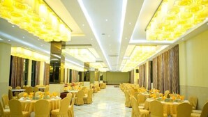 Un salón de banquetes con mesas y sillas redondas, ventanas amplias y un techo alto con iluminación decorativa.