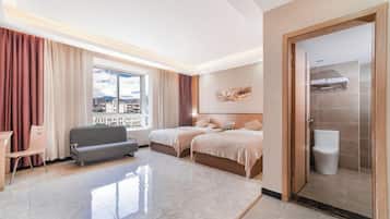 Una habitación de hotel con un ventanal grande, dos camas, un sofá, un escritorio y un baño.