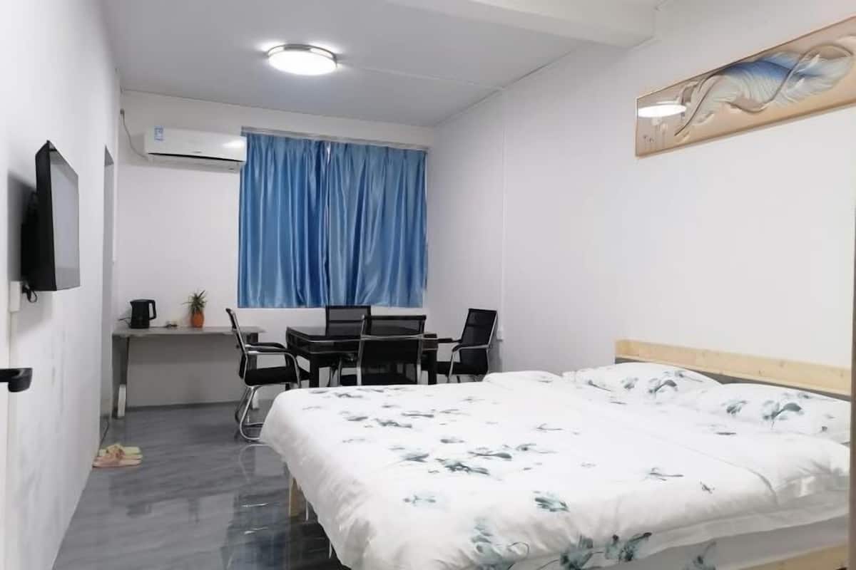 A hotel room with a bed, a desk with a chair, a television, and an air conditioning unit.