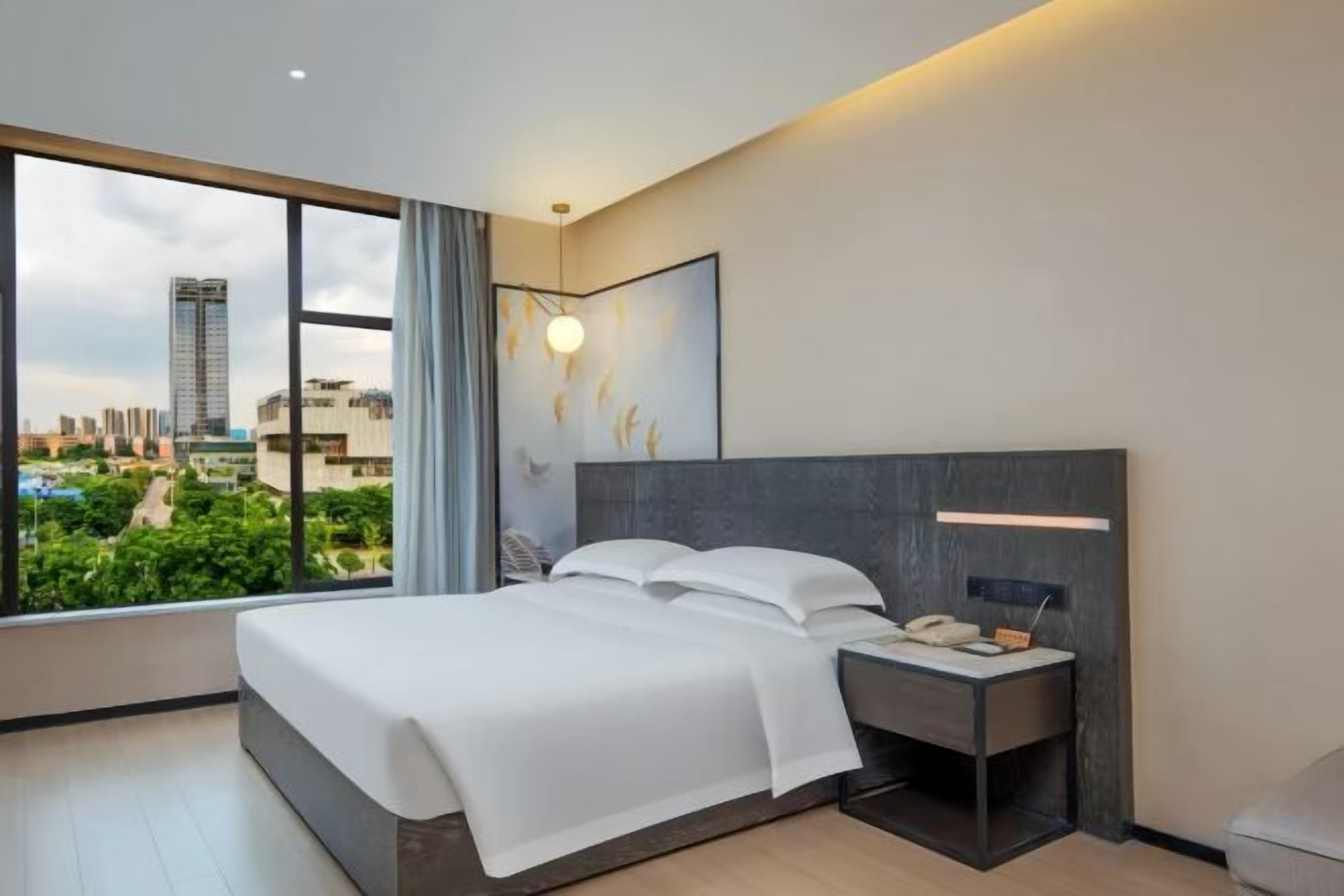 Une chambre d’hôtel moderne avec un grand lit, une table de chevet et une vue sur le paysage urbain.
