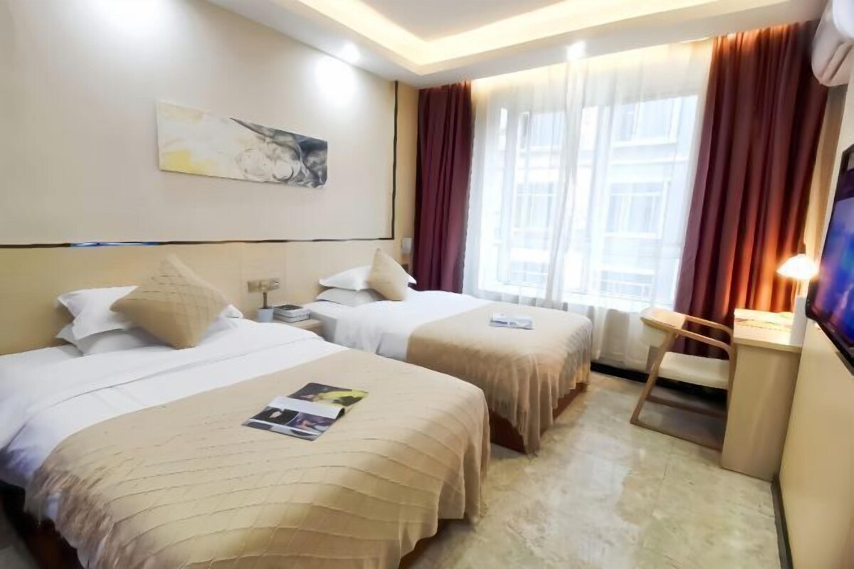 Ein Hotelzimmer mit zwei Betten, einem Schreibtisch, einem Stuhl, einem Fernseher und einem Fenster mit Vorhängen.