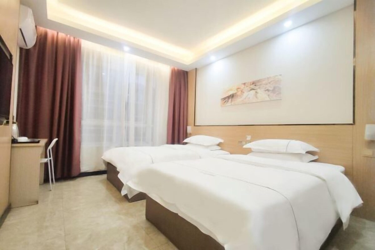 Ein Hotelzimmer mit zwei Betten, einem Schreibtisch, einem Stuhl und einem großen Fenster mit Vorhängen.