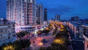 A high-rise building with multiple floors, surrounded by a cityscape with other buildings and a busy street with vehicles and pedestrians. - Yebang Convenience Hotel (Guilin North Railway Station) (Lingchuan)