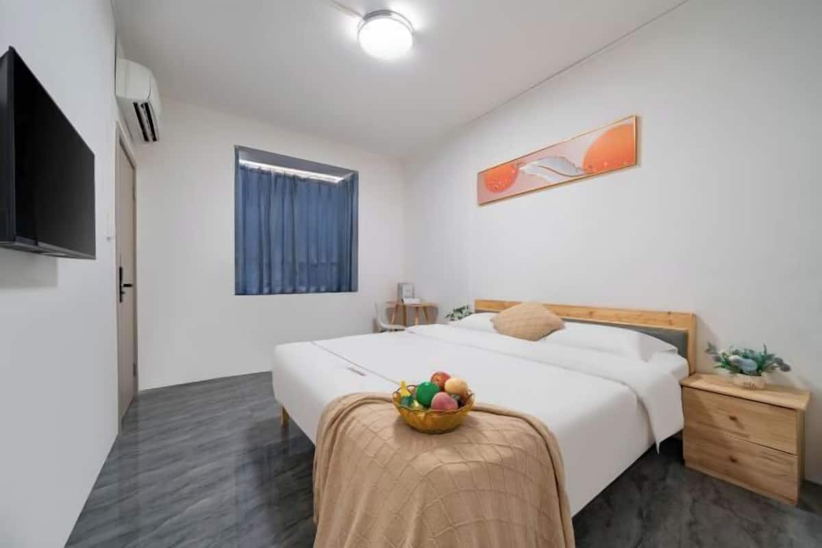 A hotel room with a bed, a bedside table, a TV, a window with curtains, and a wall-mounted artwork.
