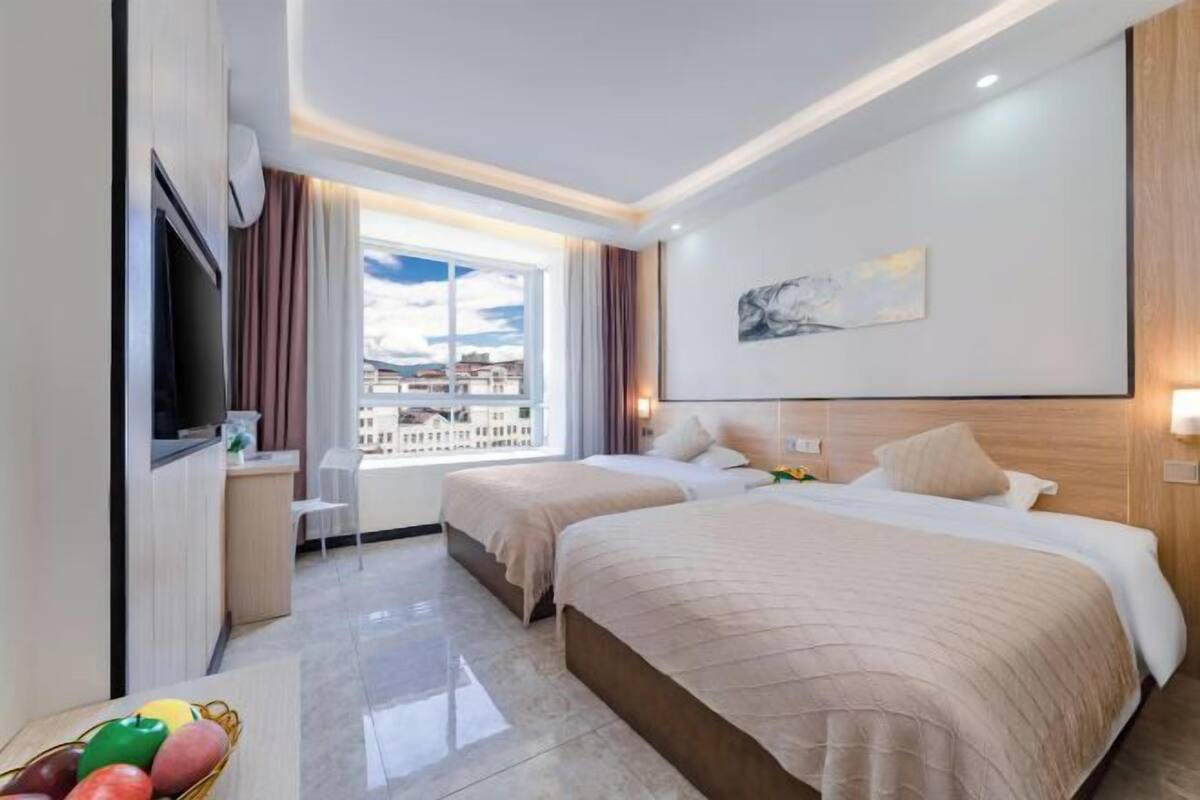 A hotel room with two beds, a TV, a window with a city view, and a painting on the wall.