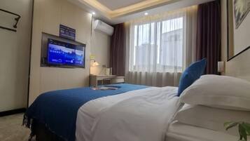 A hotel room with a bed, a TV mounted on the wall, a desk, and a window with curtains.