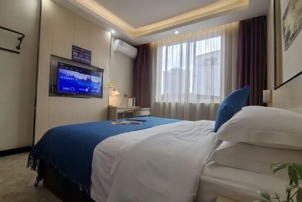 Ein Hotelzimmer mit Bett, einem an der Wand montierten Fernseher, einem Schreibtisch und einem Fenster mit Vorhängen.