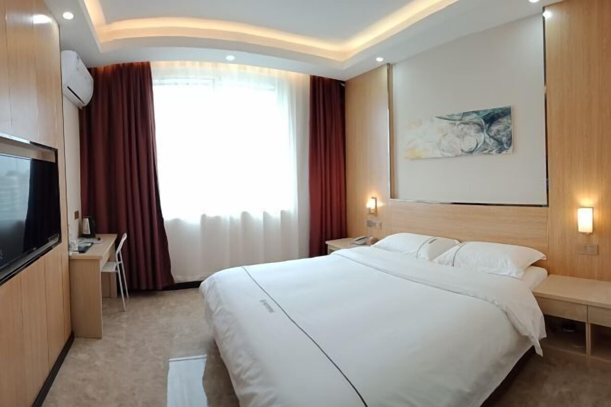 Ein Hotelzimmer mit einem großen Bett, einem Schreibtisch mit Stuhl, einem Fernseher und einem Gemälde an der Wand.