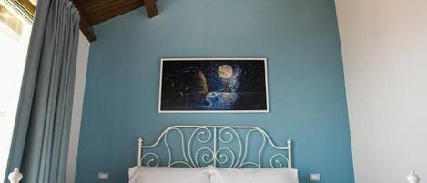 A bedroom with a white metal bed frame, a blue wall, and a painting of a moon and stars.