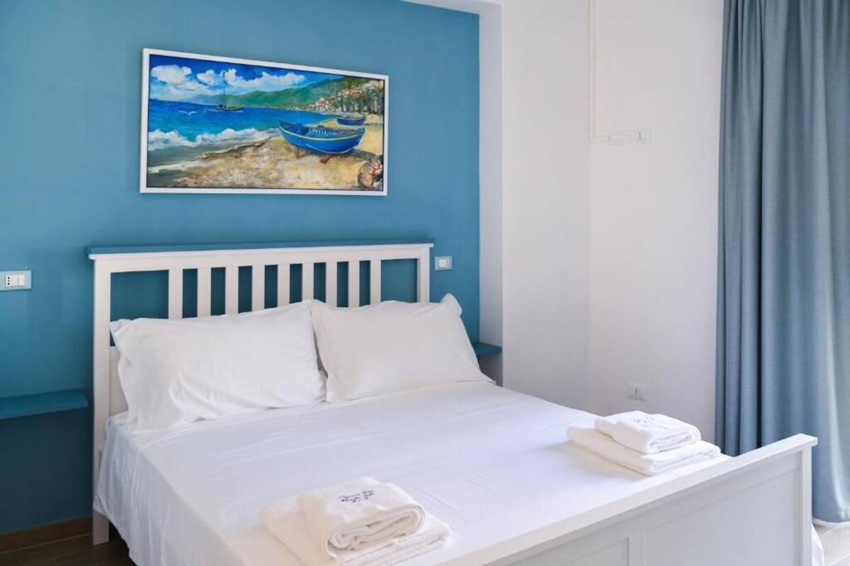 A bedroom with a white bed, white headboard, and a painting of boats on the wall.