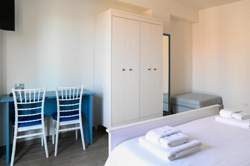 A bedroom with a bed, a wardrobe, a desk with chairs, and a small seating area.