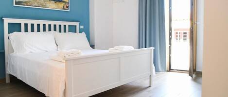 Un dormitorio con cama blanca, un cuadro en la pared y vista a través de una puerta.