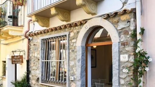 Un bâtiment en pierre doté d’un balcon, de plantes en pot et d’une enseigne indiquant la présence d’un restaurant.
