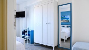 Une chambre avec une armoire blanche, un lit avec une tête de lit bleue, un bureau avec une chaise et un téléviseur fixé au mur.