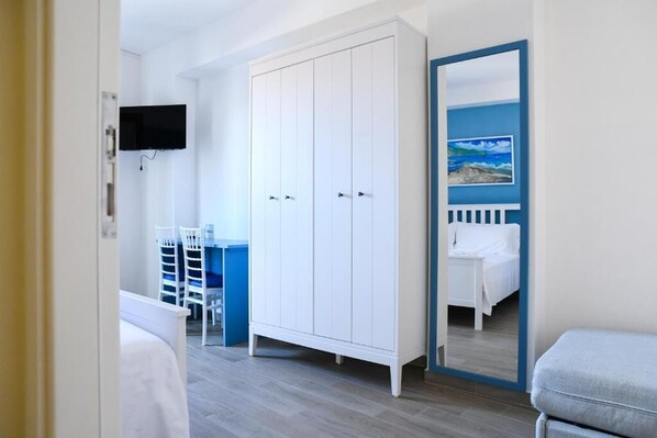 A bedroom with a white wardrobe, a bed with a blue headboard, a desk with a chair, and a TV mounted on the wall. - Signora Tita B&B Chianalea Scilla (Scilla)