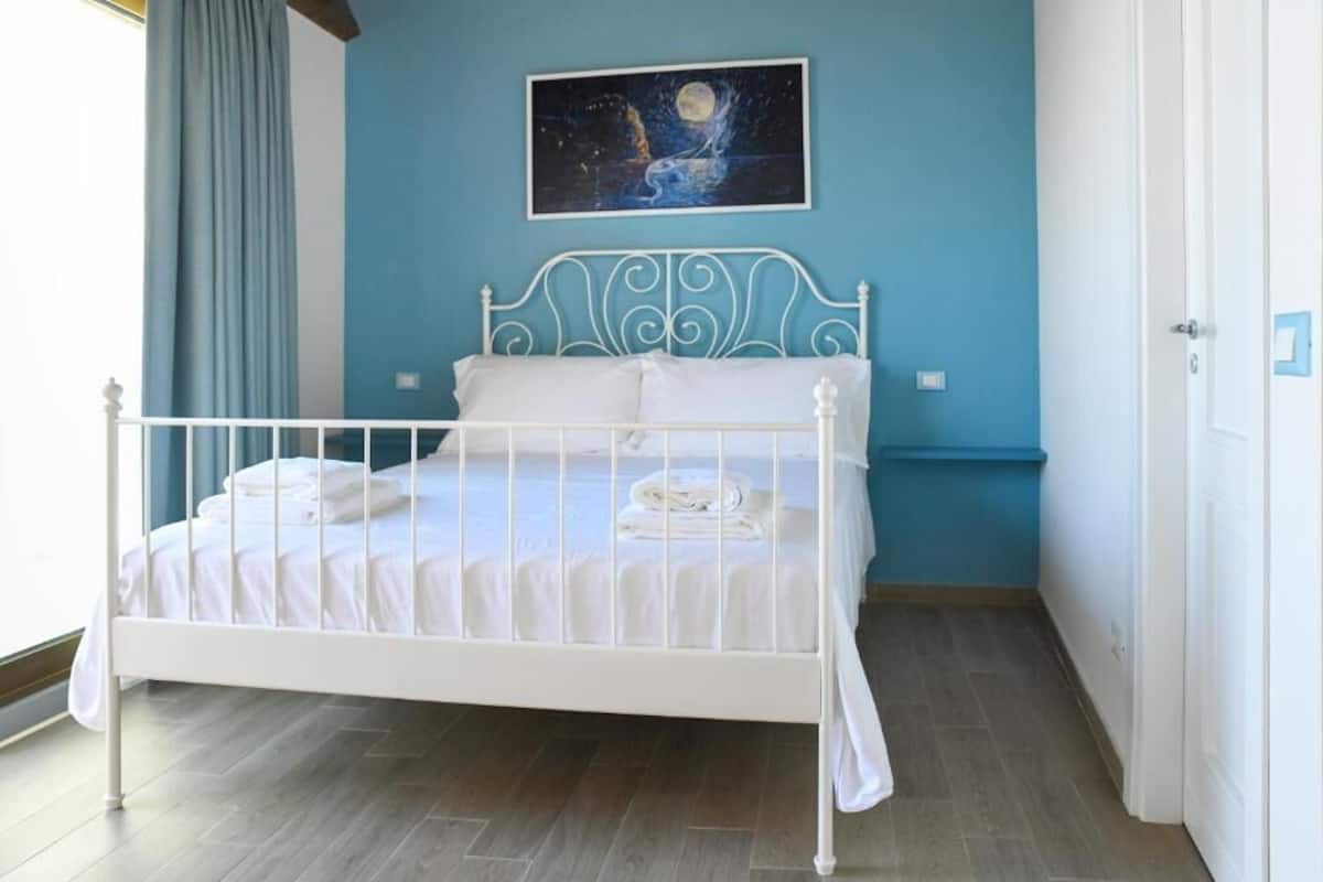 A bedroom with a white metal bed frame, a blue wall, and a painting of a night scene.