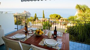A wooden table set for two with plates, glasses, and a bowl of lemons, overlooking a scenic view of the sea and greenery. - Luxury sea View, With Infinity Pool in Sicily (Cefalù)