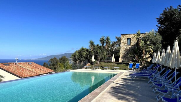 A clear blue pool with lounge chairs and umbrellas, surrounded by greenery and a stone building. - Luxury sea View, With Infinity Pool in Sicily (Cefalù)