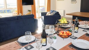 Una zona de menjador amb una taula preparada per a dues persones, una ampolla de vi i un bol de fruita.
