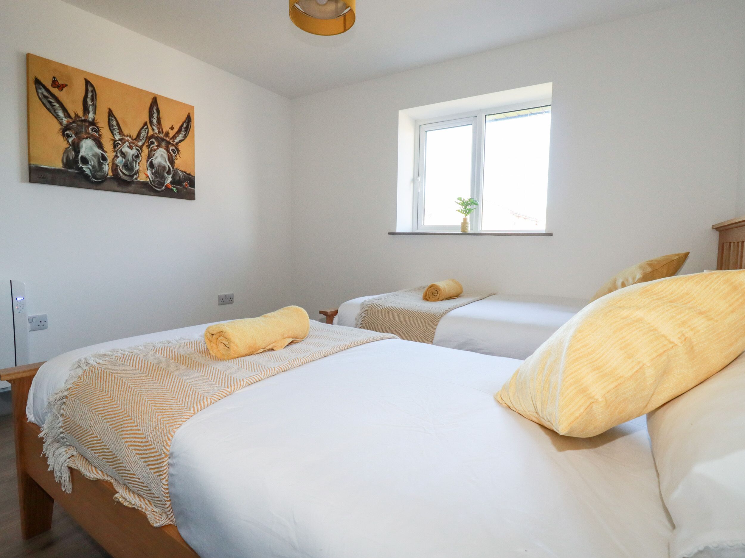 Quarto de hotel com duas camas, janela com planta e pintura de burros na parede.