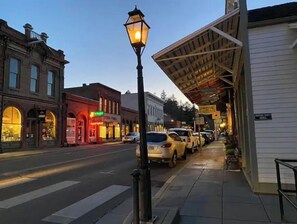 A street view at dusk with buildings, a street lamp, parked cars, and a sidewalk. - Cozy Cottage on Applegate River Micro-Farm at Vineyards.15 Min to Jacksonville (Jacksonville)