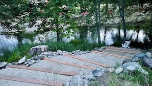 Un chemin de gravier, bordé de planches de bois et d’une bordure de pierres, mène à un banc situé au bord d’un lac.