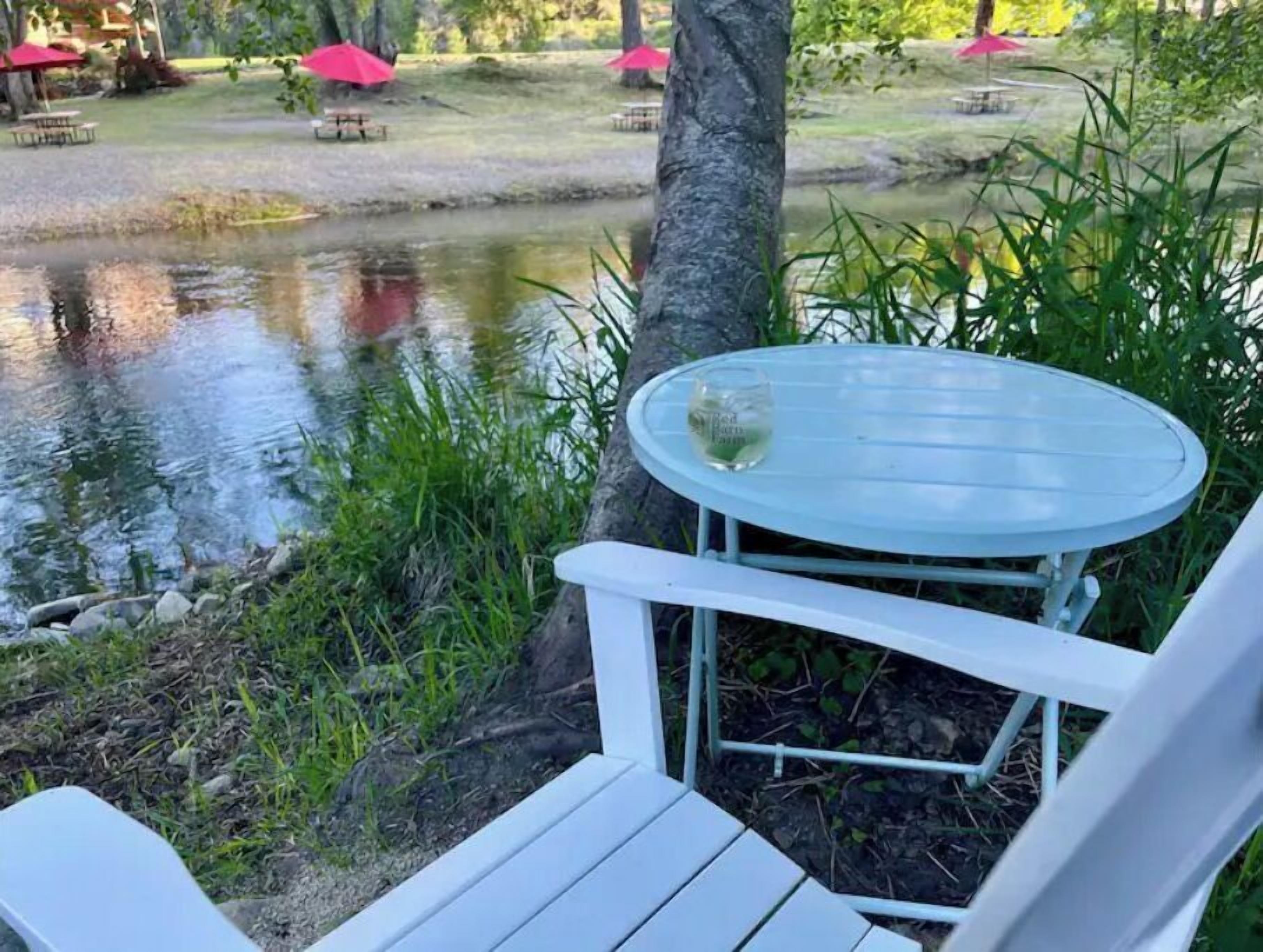 Un espace extérieur aménagé avec des sièges blancs, comprenant une table et une chaise, un verre d’eau, et un bassin en arrière-plan.