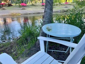 A white outdoor seating area with a table and chair, a glass of water, and a pond in the background. - Cozy Cottage on Applegate River Micro-Farm at Vineyards.15 Min to Jacksonville (Jacksonville)