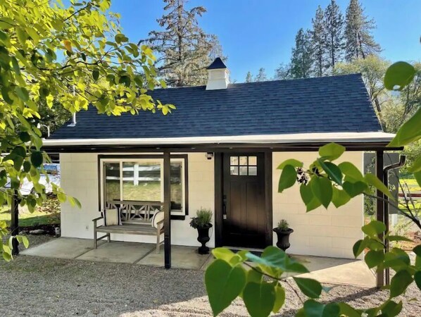 A small, single-story house with a dark roof, a front door, and a visible porch area. - Cozy Cottage on Applegate River Micro-Farm at Vineyards.15 Min to Jacksonville (Jacksonville)