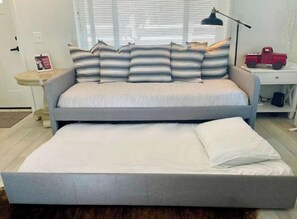 A double bed with a grey headboard and a lower single bed. There is a nightstand with a lamp and a small red toy truck. - Cozy Cottage on Applegate River Micro-Farm at Vineyards.15 Min to Jacksonville (Jacksonville)