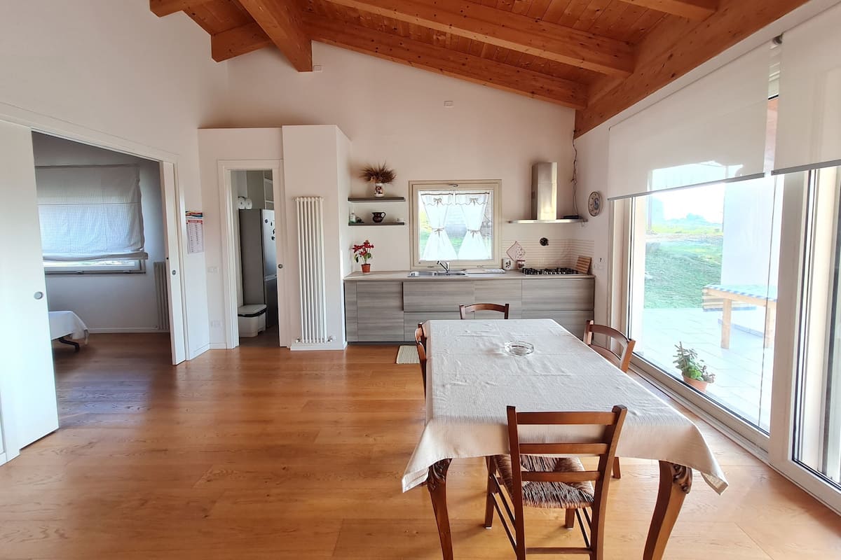 Een ruime keuken met houten balken, een eethoek met tafel en stoelen, en grote ramen met uitzicht op de omgeving.