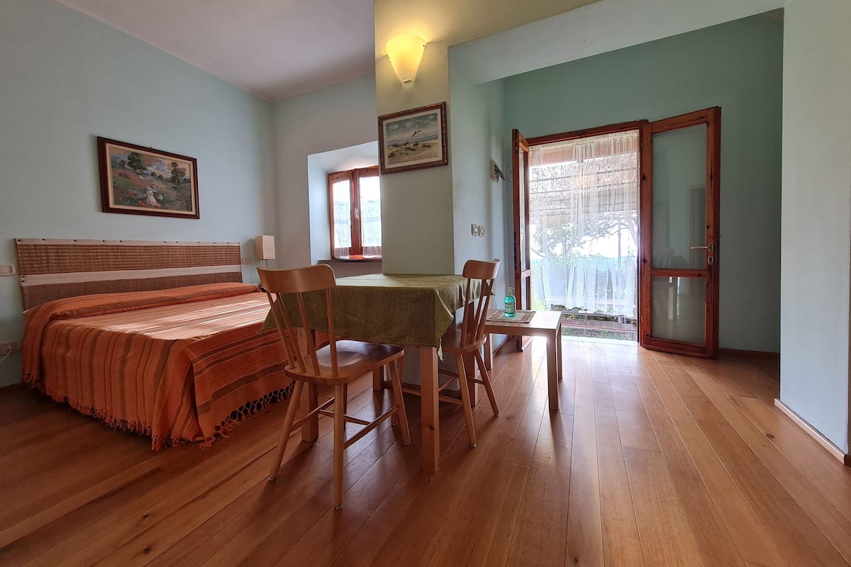 Een kamer met een bed, een tafel met stoelen, een raam met gordijnen en een deur.