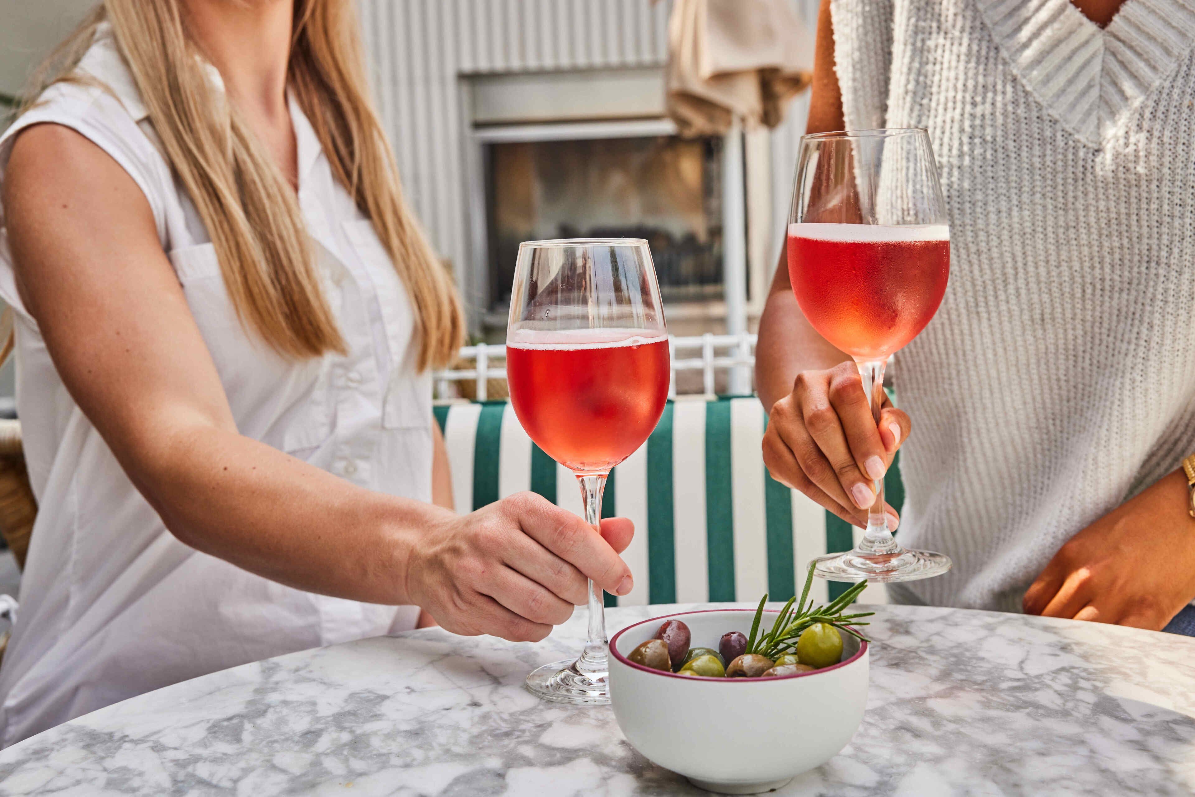 Two people holding wine glasses at a table with a bowl of olives and rosemary.