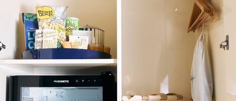 Un mini refrigerador con diversas bebidas y aperitivos, un tendedero de madera y una pequeña estantería con productos envasados.