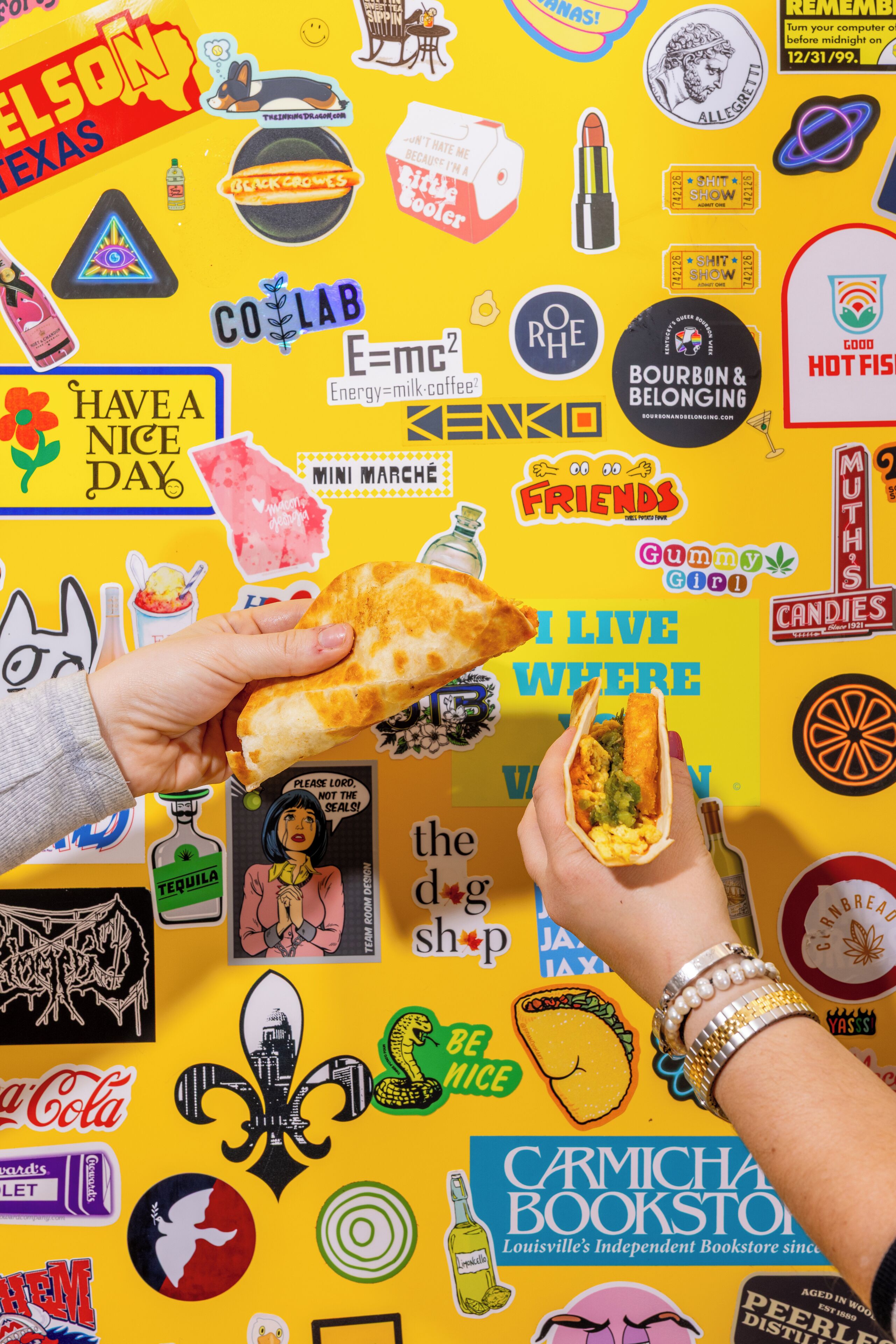 A wall covered with various stickers and posters, including brands like Coca-Cola, CoLab, and Friends.