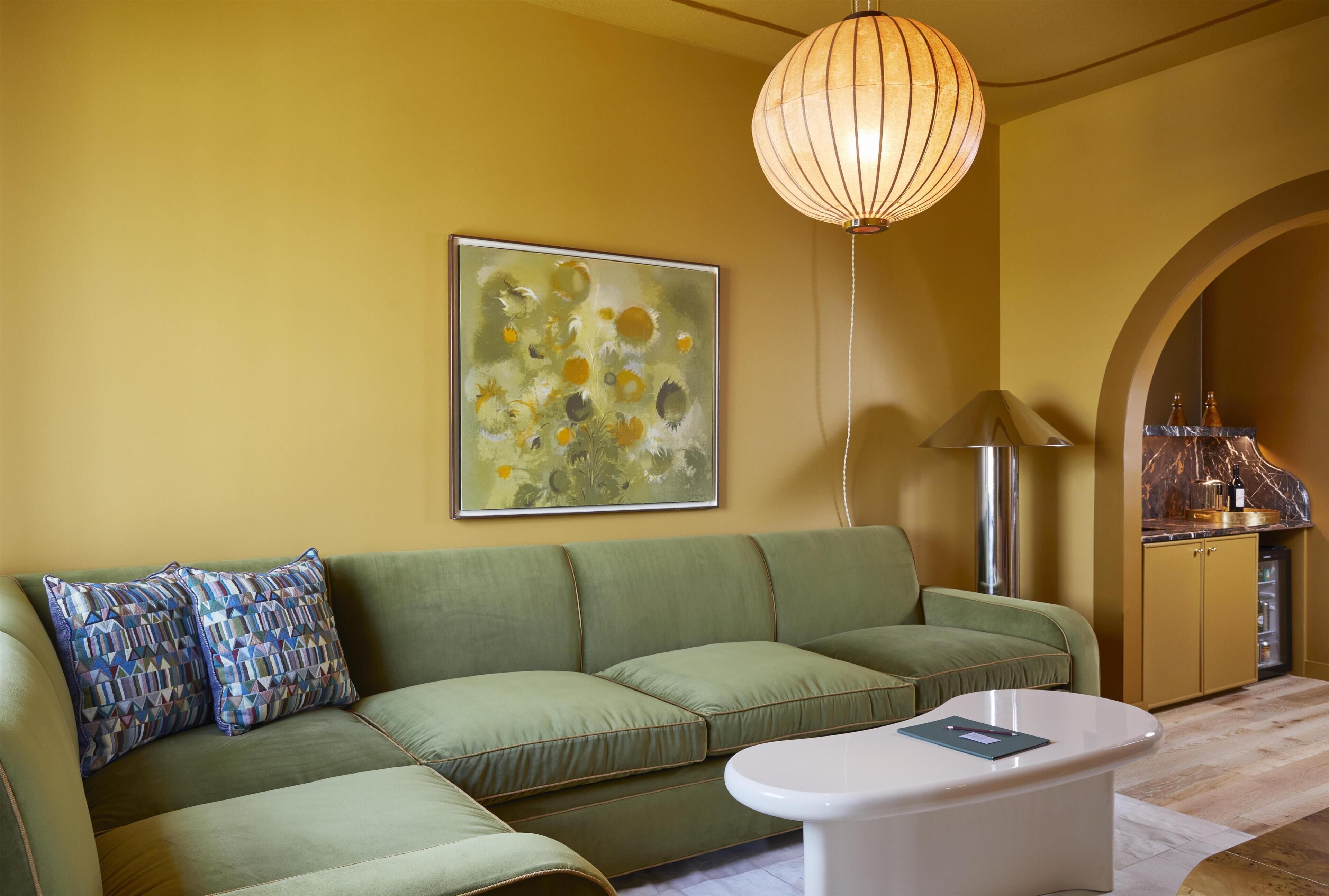 A living room with a green sofa, a white coffee table, a painting, and a pendant light.