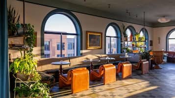A spacious lounge area with arched windows, comfortable seating, and a variety of plants.