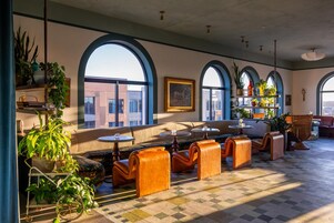 A spacious lounge area with arched windows, comfortable seating, and a variety of plants.
