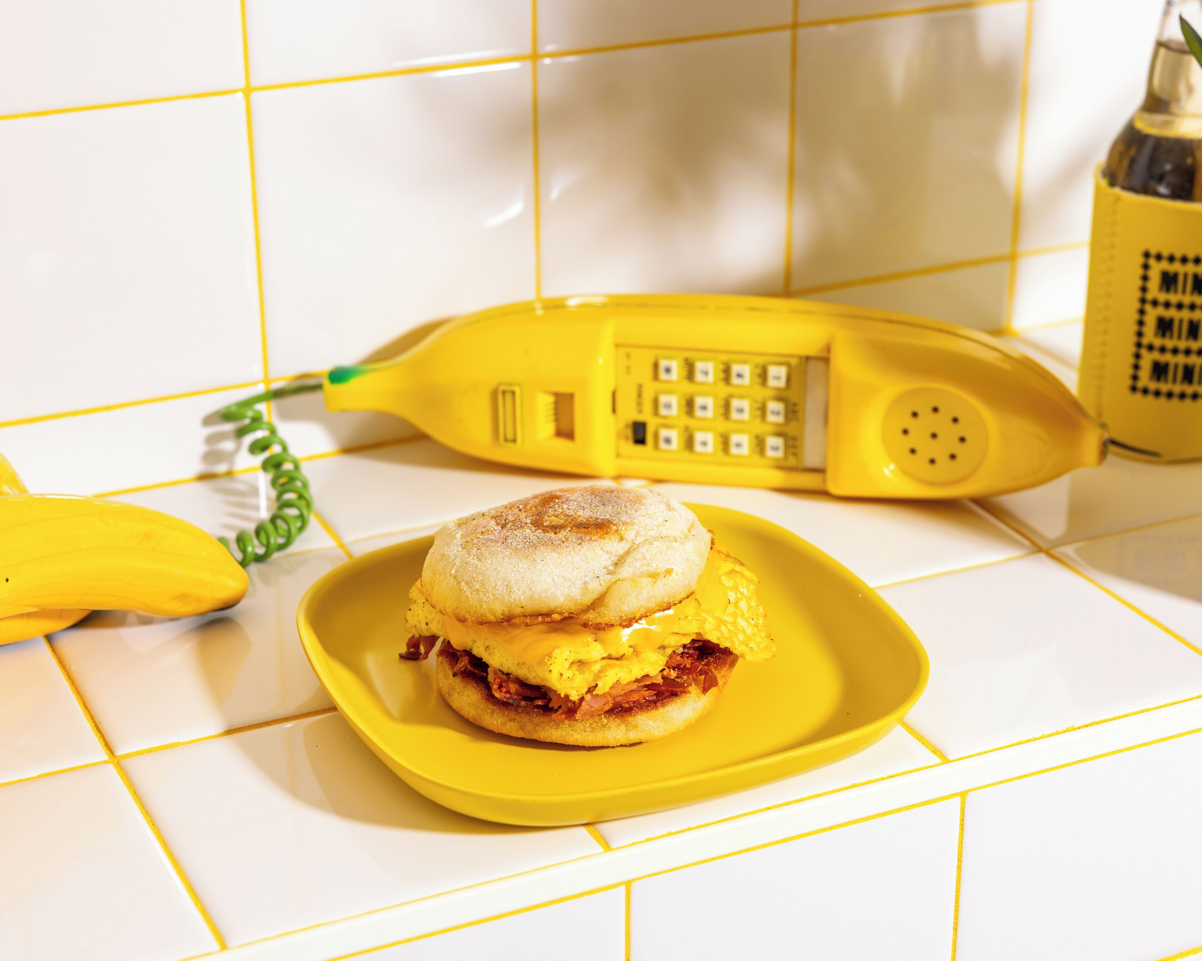 Sanduíche num prato amarelo, com um telefone amarelo e uma banana ao fundo.