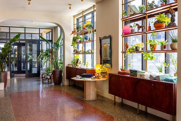 Un vestíbulo de hotel con un mostrador de recepción de madera, una zona de estar con un sofá y un ventanal con plantas en macetas.