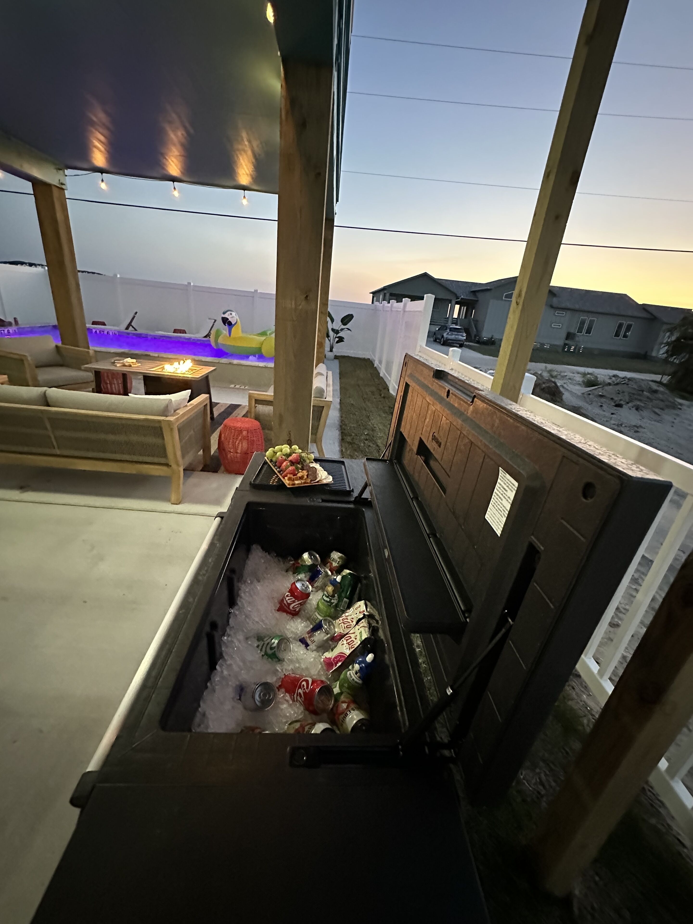 Un área de piscina con zona de estar, un refrigerador de bebidas y vistas a una casa y la playa.