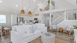 A spacious living area with a white sofa, a round coffee table, and a staircase leading to an upper level. - Reel Paradise: NEW Luxury 5BR! Private POOL + FirePit & OutdoorTV. Great Views! (Port Aransas)