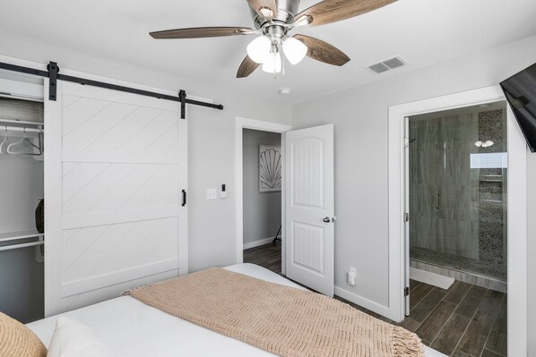 Un dormitorio con cama, ventilador de techo, puerta corredera del armario y zona de ducha.