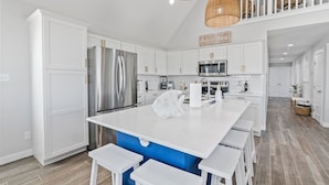 A modern kitchen with white cabinetry, stainless steel appliances, and a central island with bar stools. - Reel Paradise: NEW Luxury 5BR! Private POOL + FirePit & OutdoorTV. Great Views! (Port Aransas)
