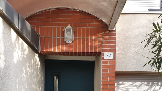 Uma porta azul escura com puxador de metal, uma pequena janela acima dela e uma placa com o número '32' na parede.