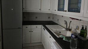Cozinha com armários brancos, bancada preta, pia e geladeira.